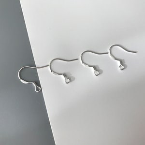 May include: Three silver earring hooks, each with a small loop at the end. The hooks are arranged in a row on a white surface.