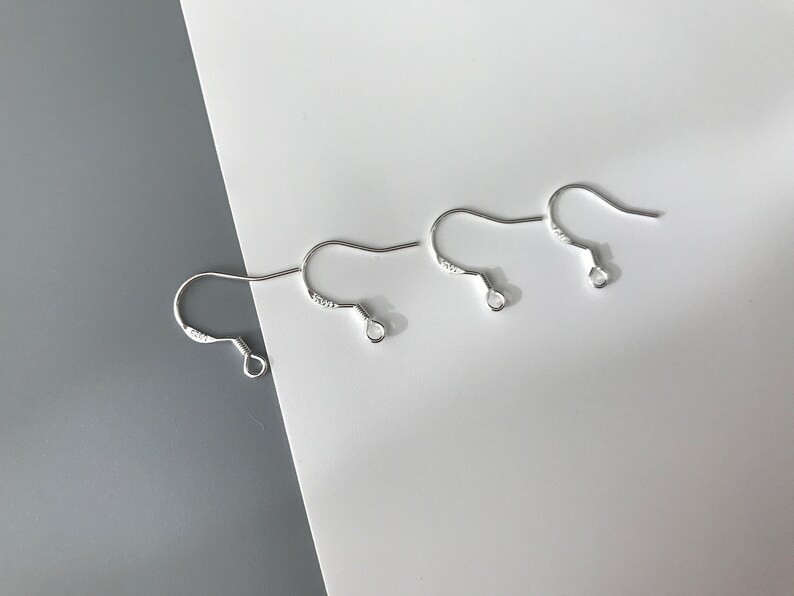 May include: Three silver earring hooks, each with a small loop at the end. The hooks are arranged in a row on a white surface.