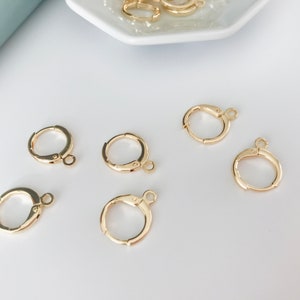 May include: Gold-toned earring hoops with a hinged closure. The hoops are arranged on a white surface.
