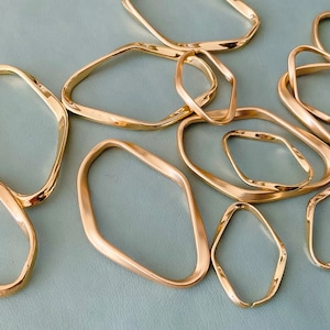 May include: A set of gold-toned metal rings with irregular, wavy shapes. The rings are arranged on a light blue surface.