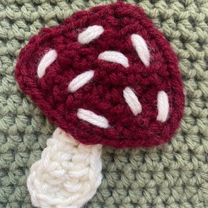 May include: A crocheted mushroom with a burgundy cap and white spots and a white stem.