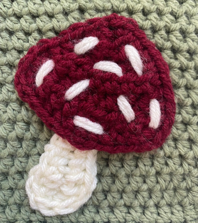 May include: A crocheted mushroom with a burgundy cap and white spots and a white stem.