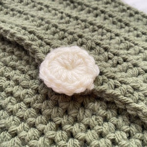 May include: A close-up of a green crocheted fabric with a white crocheted button in the center.