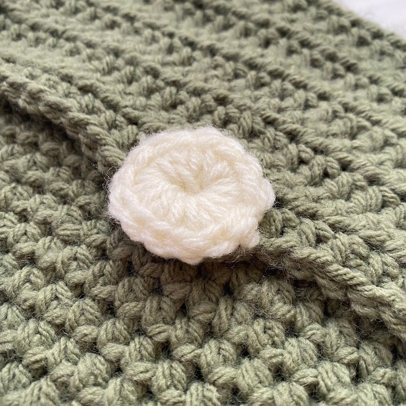 May include: A close-up of a green crocheted fabric with a white crocheted button in the center.