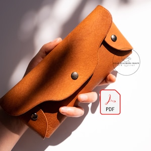 May include: A brown leather wallet with a flap closure and metal snaps. The wallet is held in a hand. The text "LEAP LEATHER CRAFT NEW ZEALAND" is visible on the wallet.