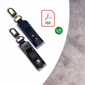 以下が含まれることがあります： 金色のキーリングが付いた革製のキーホルダー2つ。1つはネイビーブルー、もう1つはブラックです。