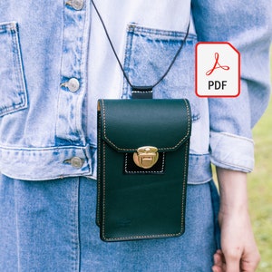 May include: A dark green leather phone case with a gold clasp and a black strap. The case is hanging from a person's shoulder.