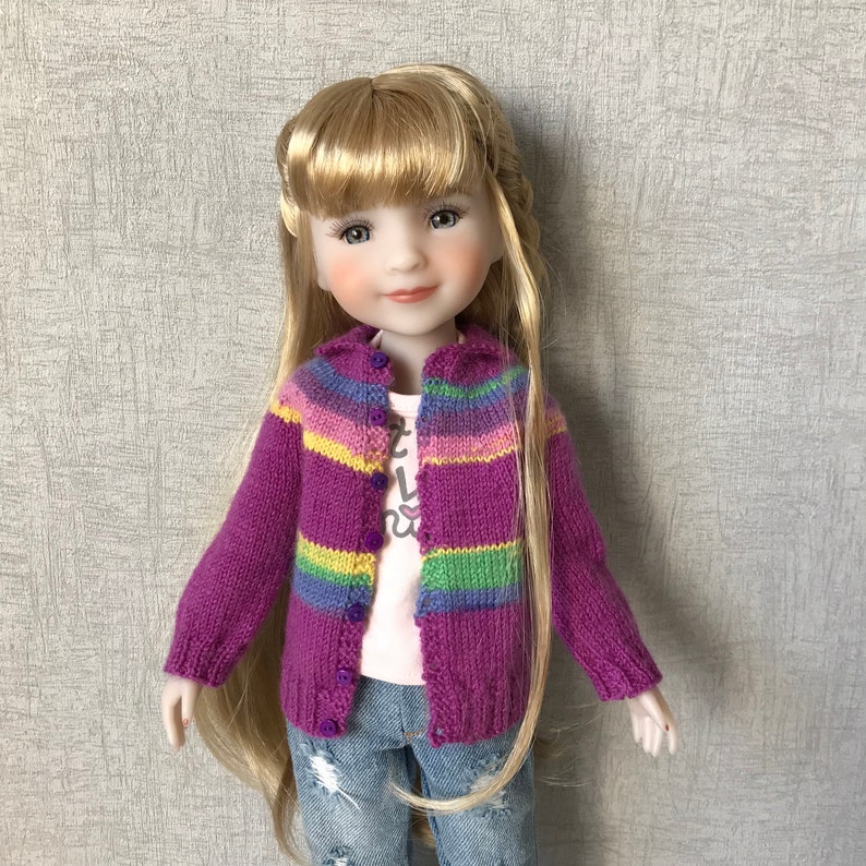 May include: A doll with long blonde hair wearing a purple and rainbow striped cardigan with a white shirt underneath and blue jeans.