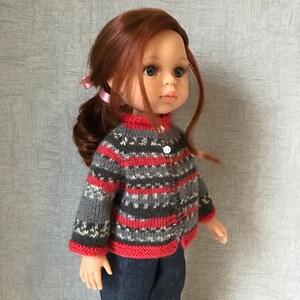 May include: A doll with red hair wearing a gray and red striped sweater with a white button. The doll is wearing blue jeans.