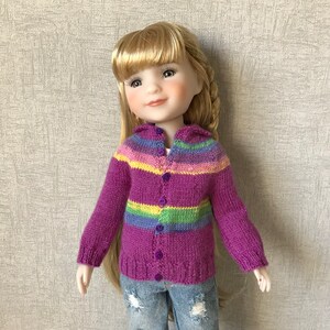 May include: A doll wearing a purple and multi-coloured striped cardigan with buttons. The cardigan has a hood and is knitted.