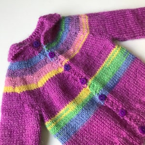May include: A purple knitted cardigan with a colourful striped pattern. The cardigan has a collar and buttons down the front.