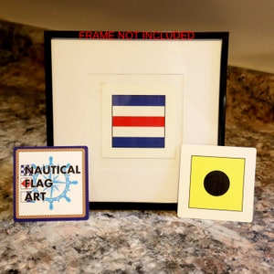 Puede incluir: Una bandera náutica enmarcada con un diseño rojo, blanco y azul. La bandera se muestra junto a una bandera amarilla con un círculo negro en el centro. El marco es negro y el paspartú es blanco. El texto "FRAME NOT INCLUDED" está impreso en la parte superior del marco. Una pequeña pegatina cuadrada con el texto "NAUTICAL FLAG ART" está en la esquina inferior izquierda de la imagen.