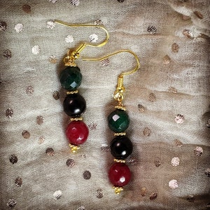 May include: A pair of dangle earrings with green, black, and red gemstone beads. The earrings have gold-toned metal hooks.