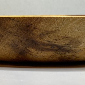 Puede incluir: Un cuenco de madera con un acabado natural de vetas. El cuenco tiene forma redondeada y una superficie lisa y pulida. La madera es de color marr&oacute;n claro c&aacute;lido con vetas marr&oacute;n oscuro.