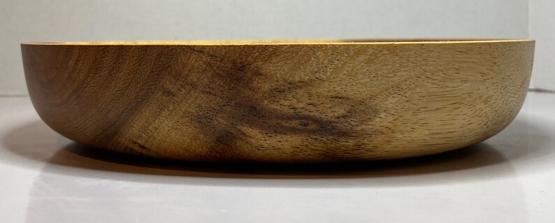 Puede incluir: Un cuenco de madera con un acabado natural de vetas. El cuenco tiene forma redondeada y una superficie lisa y pulida. La madera es de color marr&oacute;n claro c&aacute;lido con vetas marr&oacute;n oscuro.