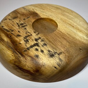 Puede incluir: Un portavelas redondo de madera con vetas naturales. Tiene una hendidura circular en el centro para una vela. La madera presenta manchas oscuras y nudos, lo que a&ntilde;ade encanto r&uacute;stico.