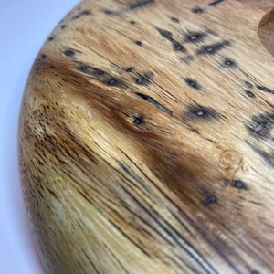 Puede incluir: Primer plano de una tabla redonda de madera para servir con un patr&oacute;n de vetas naturales. La tabla es de color marr&oacute;n claro con detalles en marr&oacute;n oscuro y negro. La veta de la madera es visible y la tabla tiene un acabado liso.