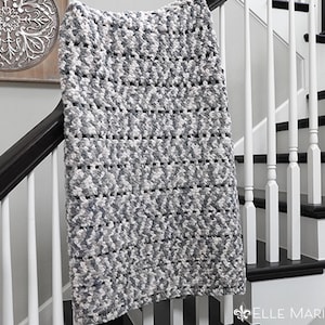 May include: A gray and white crocheted throw blanket draped over a white railing with black trim.