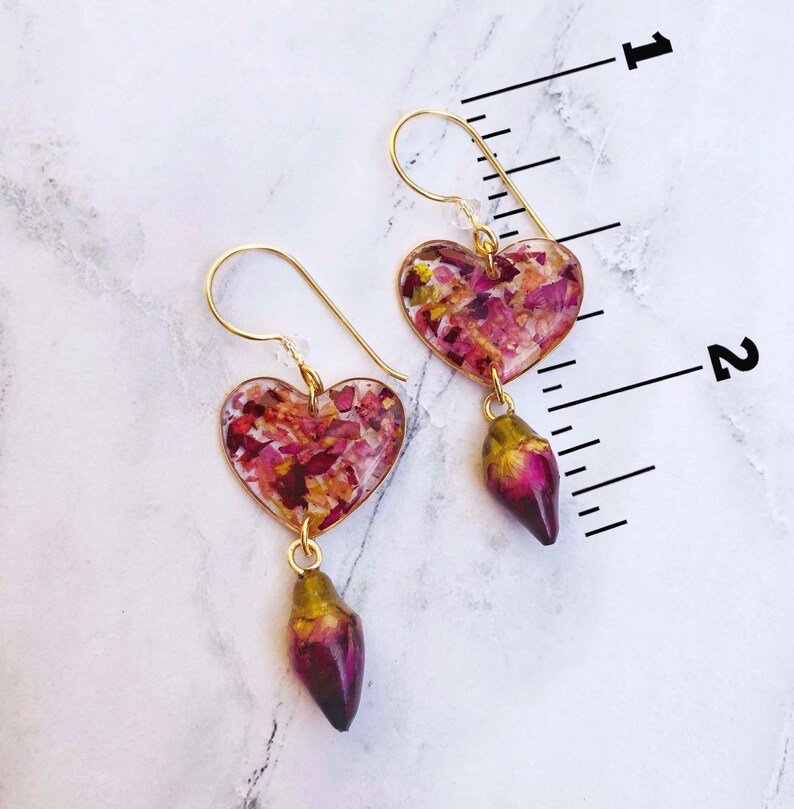 Puede incluir: Pendientes de coraz&oacute;n dorados con p&eacute;talos de rosa secos encapsulados en resina transparente. Cada pendiente tiene un encanto de capullo de rosa colgante.