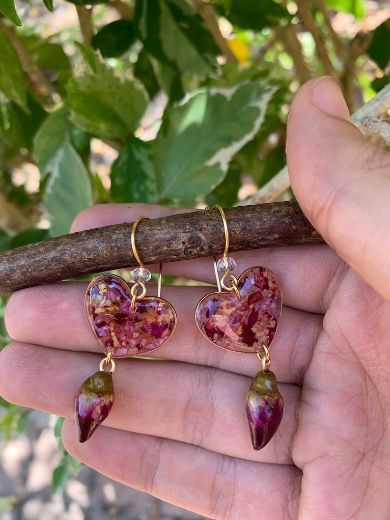 Puede incluir: Un par de pendientes de coraz&oacute;n dorados con p&eacute;talos de flores secas encapsulados en resina. Cada pendiente tiene un colgante en forma de l&aacute;grima con un dise&ntilde;o similar.