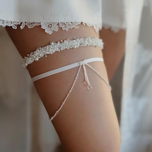 May include: White bridal garter with a beaded band and a delicate chain with crystal accents.
