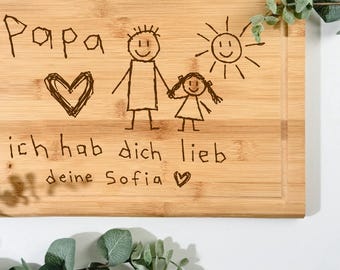 Pode incluir: Tábua de corte retangular de madeira com uma ranhura ao redor da borda. A tábua apresenta um desenho de uma família de bonecos de palito, um coração e as palavras "Papa, ich hab dich lieb, deine Sofia" em preto.