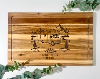 Pode incluir: Tábua de corte retangular de madeira com uma cena de acampamento gravada. O design apresenta uma autocaravana, montanhas, árvores e uma fogueira. O texto "LAURA & TOBIAS ON TOUR" está abaixo. A tábua tem um sulco para suco ao redor da borda.