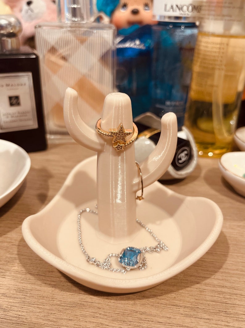 K&ouml;nnte beinhalten: Wei&szlig;er Keramik-Kaktus-Ringst&auml;nder mit einem sternf&ouml;rmigen Ring und einem blauen Edelstein-Armband.