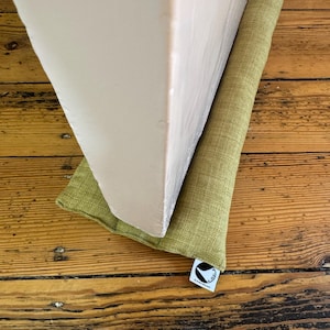 May include: A green doorstop with a white label that says "Doormat" is placed at the bottom of a white door frame. The doorstop is on a wooden floor.