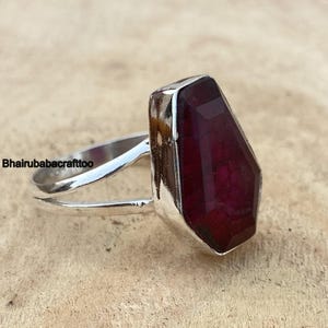 May include: A silver ring with a large, faceted, dark red gemstone. The ring has a simple, open band design.