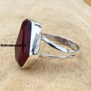 May include: A silver ring with a large, dark red gemstone. The gemstone is faceted and has a hexagonal shape. The ring band is thin and has a simple design.