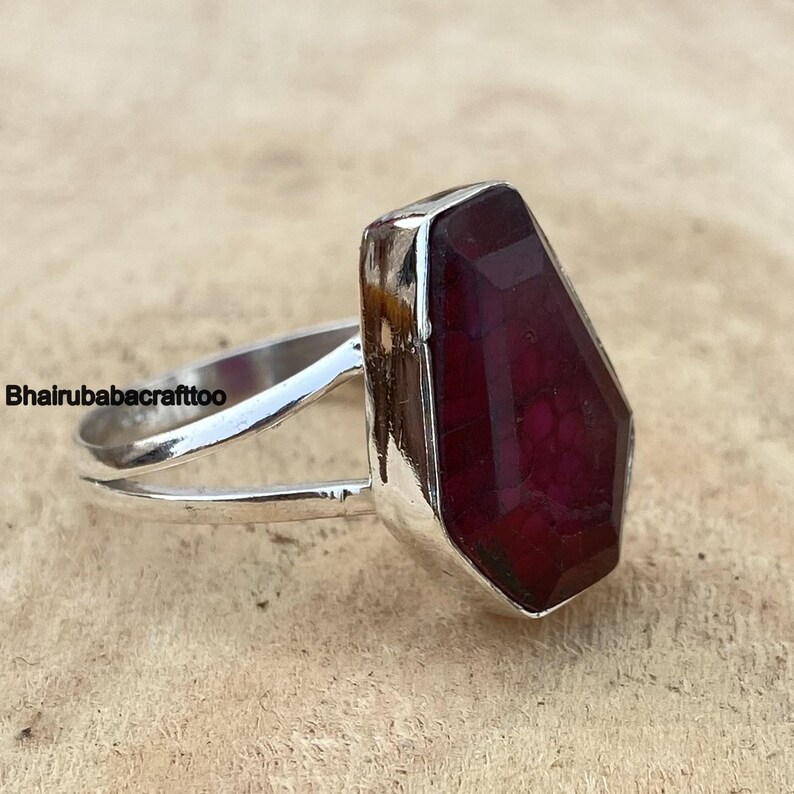 May include: A silver ring with a large, faceted, dark red gemstone. The ring has a simple, open band design.