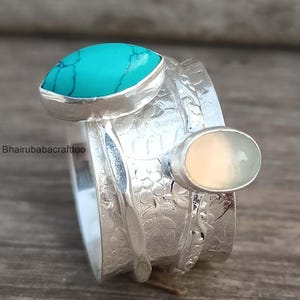 May include: A silver ring with a turquoise and a white opal stone. The ring has a textured band with a floral design.