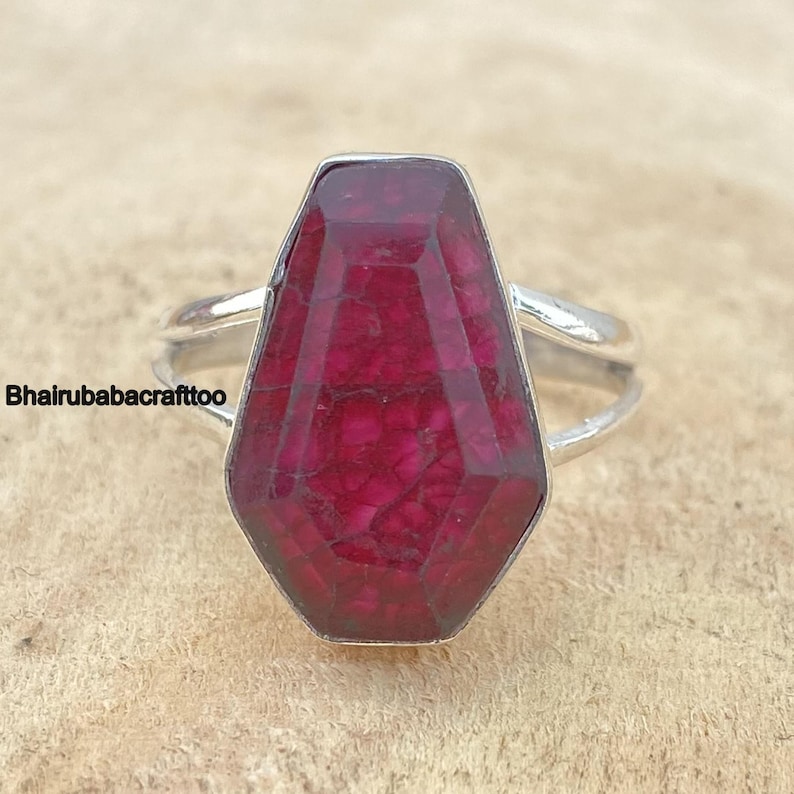 May include: A silver ring with a large, faceted, red ruby gemstone. The ruby is set in a bezel setting and has a unique, geometric shape.