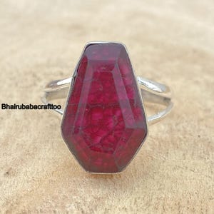 May include: A silver ring with a large, faceted, red ruby gemstone. The ruby is set in a bezel setting and has a unique, geometric shape.