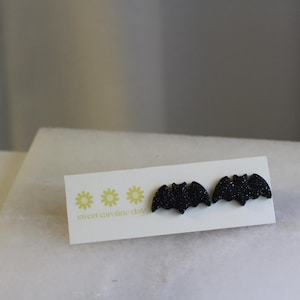 May include: A pair of black glitter bat earrings on a white card with the text "sweet caroline designs".