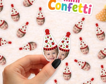 May include: A collection of small, die-cut paper confetti pieces featuring a printed photograph of a child's face wearing a white party hat decorated with red ladybugs and a red pom-pom. The text mini Confetti is displayed in colorful letters.