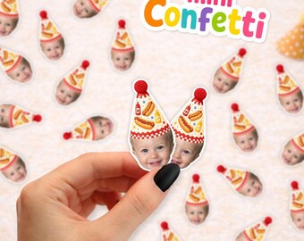 May include: Custom mini confetti pieces featuring a child's face wearing a party hat with a hot dog and mustard pattern. The confetti is scattered across the surface, with one piece held up to show the detail of the printed design.