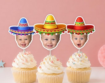 May include: Three cupcakes topped with personalized photo cake toppers. Each topper features a baby's face wearing a colorful sombrero in blue, yellow, or red, decorated with geometric patterns and small pom-poms on the brim edges.