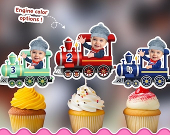 Puede incluir: Tres adornos imprimibles para cupcakes con trenes de dibujos animados en verde claro, rojo y azul oscuro, etiquetados con los números 3, 2 y 4. Cada tren incluye un recorte de un bebé con gorro de punto gris. Texto: 5 sizes, Any Skin, Any Age, 24 Hour Delivery, Engine color options, PRINTABLE CUPCAKE TOPPERS.