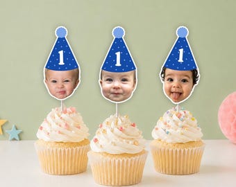 May include: Three cupcakes with white frosting and colorful sprinkles, each topped with a custom paper topper featuring a baby's face wearing a blue party hat with white stars and the number one printed in white on the front of the hat.