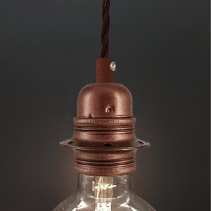 Peut inclure: Un luminaire de couleur cuivre avec une base décorative à nervures et un dessus rond et plat. Le luminaire est suspendu à un cordon noir.