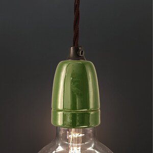 Op de afbeelding: Een groene keramische lampfitting met een zwart snoer dat eraan hangt. De fitting is ontworpen om een ​​lamp te houden.