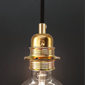 Op de afbeelding: Een gouden metalen lamp met een zwart snoer. De lamp heeft een ronde, geribbelde basis en een decoratieve ring rond de bovenkant.