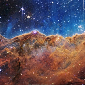 May include: A vibrant image of the Carina Nebula, showcasing a celestial landscape of glowing gas and dust. The image features shades of orange, brown, and blue, with numerous bright stars scattered throughout the scene. The nebula's formations resemble mountains.