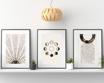 May include: Three framed art prints with black frames on a white shelf. The prints feature abstract designs in beige, black, and gold. A woven pendant light hangs above the shelf. Small potted plants are placed on the shelf.