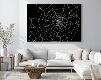 Op de afbeelding: Een groot canvas kunstwerk met een wit spinnenwebontwerp tegen een zwarte achtergrond. Het kunstwerk wordt weergegeven boven een witte hoekbank in een woonkamer. De ingewikkelde lijnen van het web creëren een opvallend contrast.