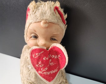 May include: A plush toy shaped like a baby holding a red heart that says "I cannot help to be so loved".