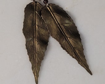 May include: A pair of gold leaf earrings with brown bead accents. The leaves are detailed with veins and have a slightly textured surface.