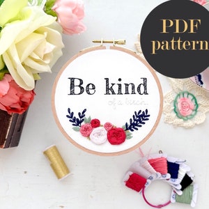 May include: Embroidery hoop with a white background and the text "Be kind of a witch..." in black. The hoop is decorated with a floral design in pink, red, white, and green.